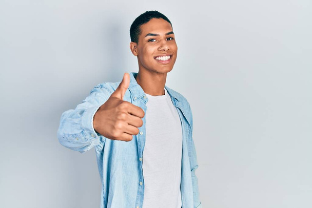 Mladý Afroameričan v neformálním oblečení dělá šťastné gesto rukou nahoru. schválení výrazu při pohledu na fotoaparát, který vykazuje úspěch.  - Fotografie, Obrázek