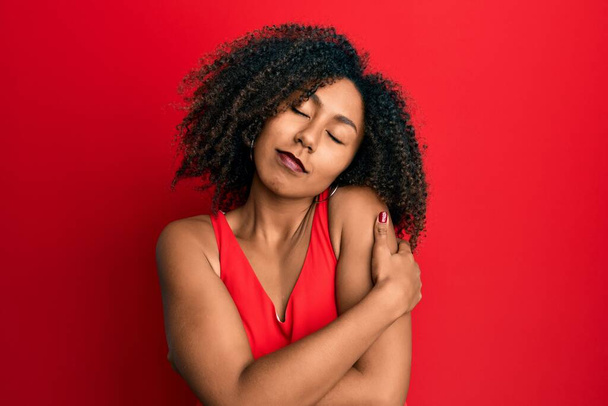 Beautiful african american woman with afro hair wearing casual clothes hugging oneself happy and positive, smiling confident. self love and self care  - Photo, Image