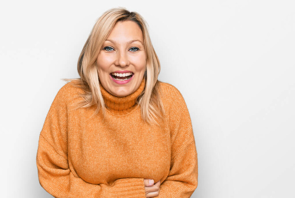 Mujer caucásica de mediana edad que usa suéter de invierno casual sonriendo y riendo en voz alta porque divertida broma loca con las manos en el cuerpo.  - Foto, imagen