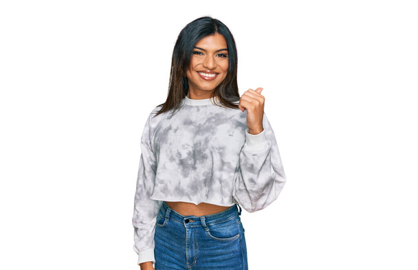 Joven transexual latina transgénero vistiendo ropa casual sonriendo con la cara feliz mirando y señalando a un lado con el pulgar hacia arriba.  - Foto, Imagen