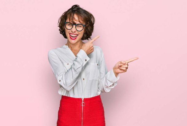 Junge hispanische Frau mit Businessstil und Brille, die lächelnd in die Kamera blickt und mit zwei Händen und Fingern zur Seite zeigt.  - Foto, Bild