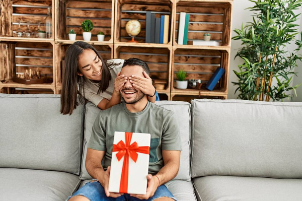 Jeune femme surprenant son petit ami avec cadeau d'anniversaire à la maison. - Photo, image