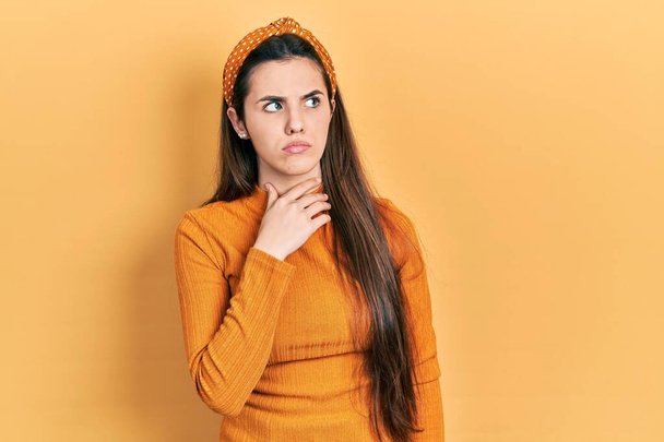 Giovane adolescente bruna con un maglione giallo casuale che tocca il collo dolorante, mal di gola per influenza, zolle e infezioni  - Foto, immagini