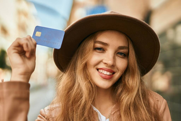 Joven chica rubia sonriendo feliz celebración de la tarjeta de crédito en la ciudad. - Foto, imagen