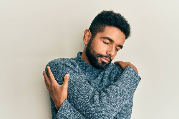 Handsome hispanic man with beard wearing casual clothes hugging oneself happy and positive, smiling confident. self love and self care  - 写真・画像