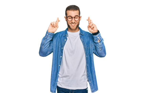 Young caucasian man wearing casual clothes gesturing finger crossed smiling with hope and eyes closed. luck and superstitious concept.  - Photo, Image