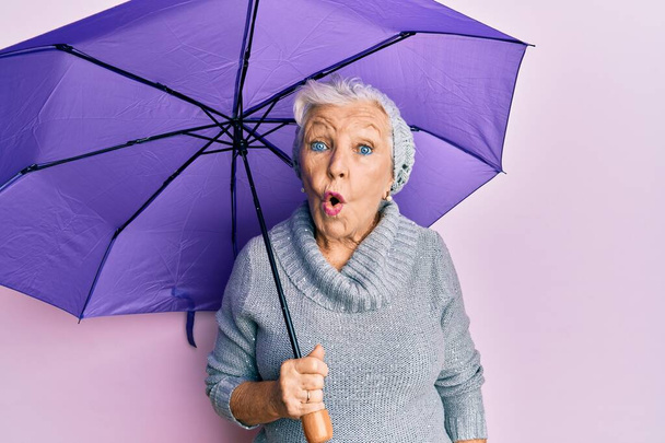 Senior harmaa tukka nainen tilalla violetti sateenvarjo peloissaan ja hämmästynyt suu auki yllätys, epäusko kasvot  - Valokuva, kuva
