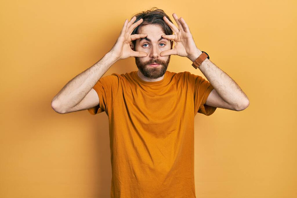 Caucasian man with beard wearing casual yellow t shirt trying to open eyes with fingers, sleepy and tired for morning fatigue  - Zdjęcie, obraz