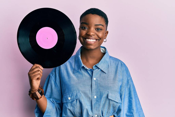 Young african american woman holding vinyl disc looking positive and happy standing and smiling with a confident smile showing teeth  - Фото, зображення