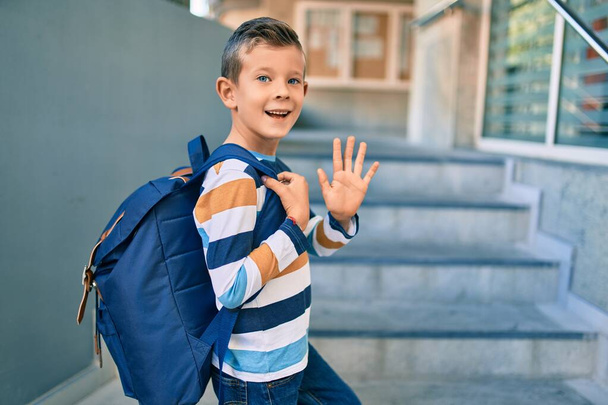 Adorable caucasian student boy smiling happy saying goodbye at the school. - 写真・画像