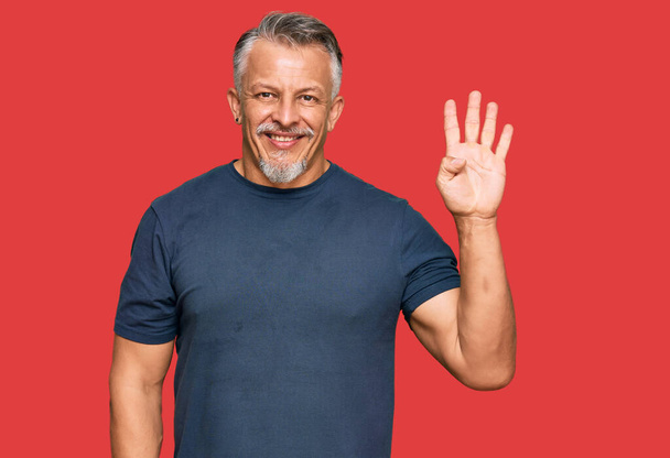 Hombre de pelo gris de mediana edad vistiendo ropa casual mostrando y señalando con los dedos número cuatro mientras sonríe confiado y feliz.  - Foto, imagen