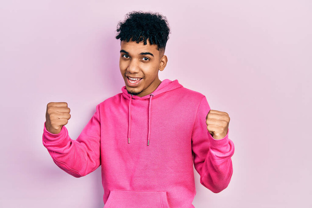 Young african american man wearing casual sweatshirt screaming proud, celebrating victory and success very excited with raised arms  - Photo, Image