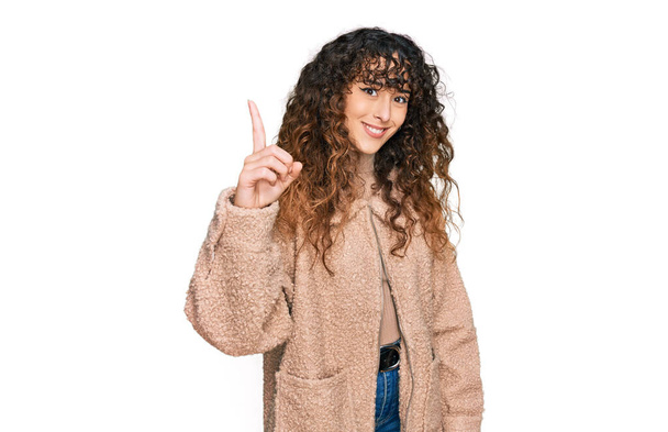 Young hispanic girl wearing winter clothes showing and pointing up with finger number one while smiling confident and happy.  - Foto, afbeelding