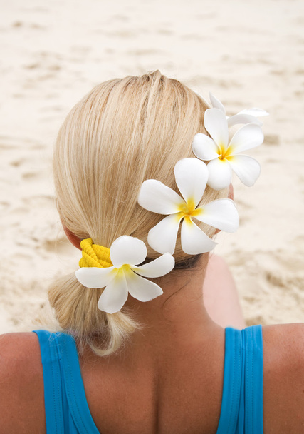 Close-up de mulher sentada na praia com flores no cabelo olhando para o mar
 - Foto, Imagem
