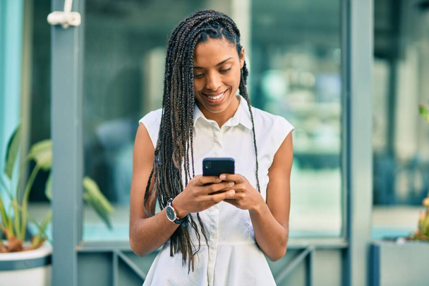 Young african american woman smiling happy using smartphone at the city. - Foto, Bild