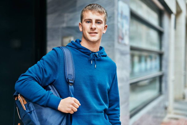 Young blond student smiling happy standing at the university. - 写真・画像