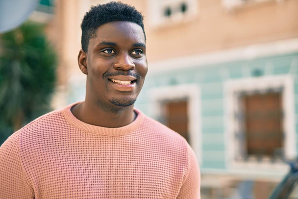 Jonge Afro-Amerikaanse man glimlachend blij staande in de stad. - Foto, afbeelding