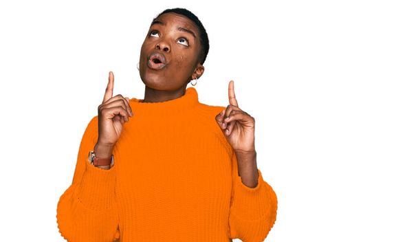 Jeune femme afro-américaine portant des vêtements décontractés étonné et surpris regardant vers le haut et pointant avec les doigts et les bras levés.  - Photo, image