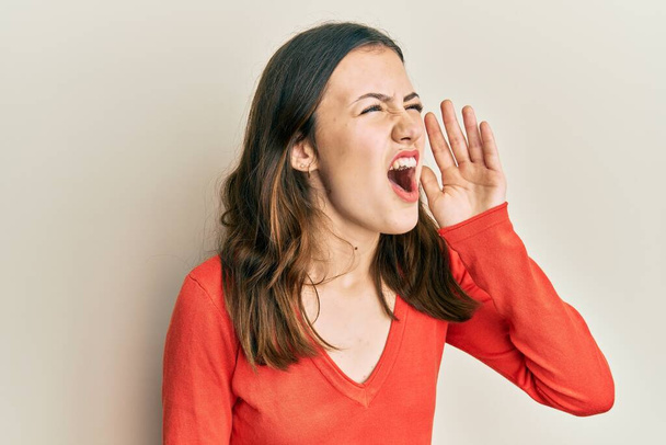 Giovane donna bruna che indossa vestiti casual urlando e urlando forte a lato con mano sulla bocca. concetto di comunicazione.  - Foto, immagini