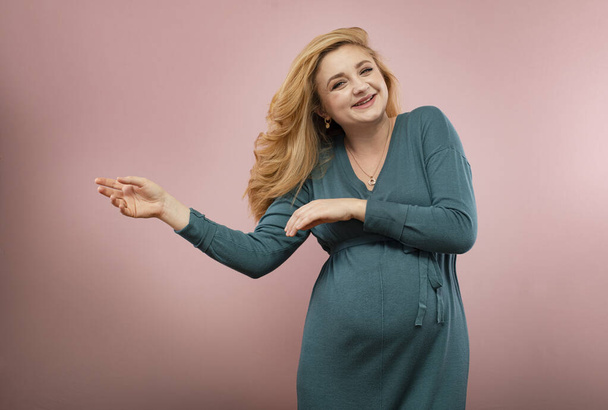 Happy pregnant woman in a green dress isolated on pink - Photo, Image