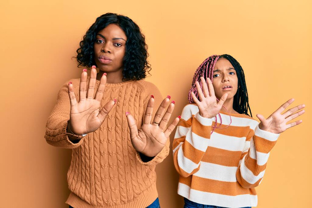 Krásná africká americká matka a dcera nosí vlněný zimní svetr pohybující se dlaněmi ukazující odmítnutí a popírání s ustrašeným a nechutným výrazem. zastavit a zakázat.  - Fotografie, Obrázek