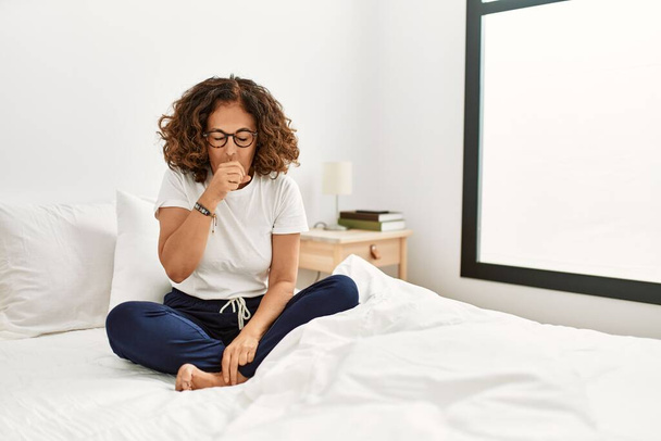 中年のパニック女性が自宅で気分が悪くベッドに座って、風邪や気管支炎の症状として咳をします。ヘルスケアの概念.  - 写真・画像