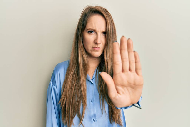 Mulher loira jovem vestindo camisa azul casual fazendo parar de cantar com palma da mão. expressão de advertência com gesto negativo e grave no rosto.  - Foto, Imagem