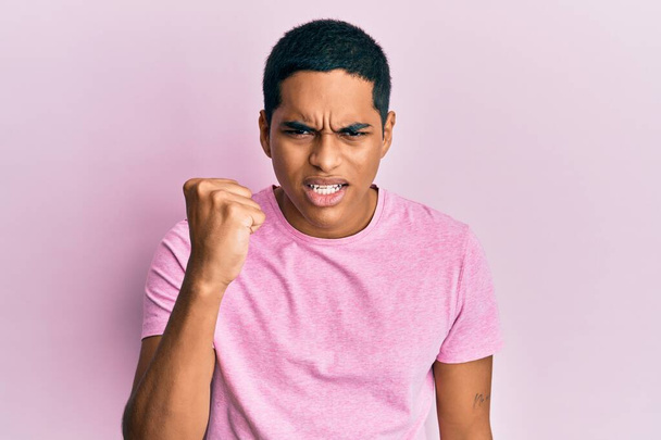 Homem hispânico bonito jovem vestindo camisa casual rosa t irritado e louco levantando punho frustrado e furioso enquanto gritando com raiva. raiva e conceito agressivo.  - Foto, Imagem