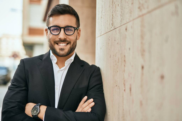 Joven empresario hispano con los brazos cruzados sonriendo feliz en la ciudad. - Foto, imagen