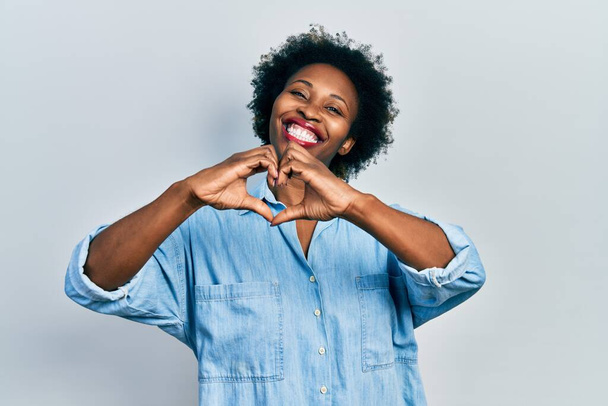 Mladá afro-americká žena nosí ležérní oblečení, usmívá se v lásce, ukazuje symbol srdce a tvar s rukama. romantický koncept.  - Fotografie, Obrázek