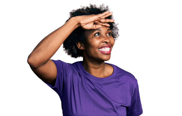 アフロの髪をしたアフリカ系アメリカ人の女性は、カジュアルな紫色のTシャツを着て、頭の上に手で遠くを見て非常に幸せと笑顔。検索の概念.  - 写真・画像