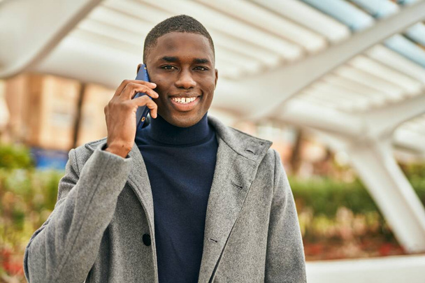 Mladý africký Američan se šťastně usmívá mluvit na smartphone ve městě - Fotografie, Obrázek