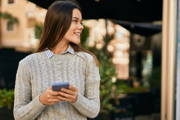 Молода іспаномовна дівчина посміхається щасливим використанням смартфона в місті
. - Фото, зображення