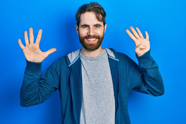 Kaukaski mężczyzna z brodą w luźnej bluzie pokazuje i wskazuje palcami numer dziewięć uśmiechając się pewny siebie i szczęśliwy.  - Zdjęcie, obraz