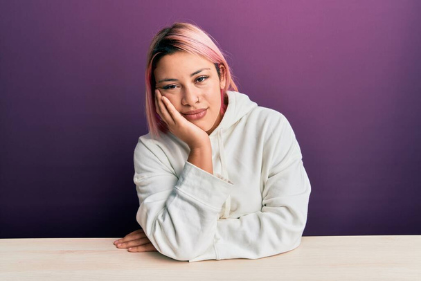 Hispanic woman with pink hair wearing casual sweatshirt sitting on the table thinking looking tired and bored with depression problems with crossed arms.  - Foto, immagini