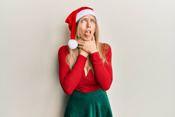 Красивая белая женщина в рождественском костюме и шляпе кричит и задыхается, потому что болезненно душит. проблемы со здоровьем. Концепция асфиксии и самоубийства.  - Фото, изображение