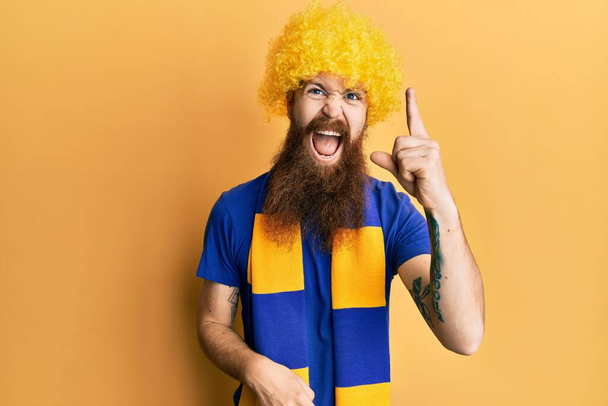 Homme rousse avec une longue barbe football hooligan jeu acclamation portant perruque drôle pointant du doigt avec une idée réussie. Sorti et heureux. numéro un.  - Photo, image