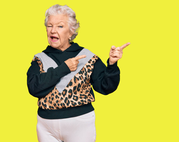 Senior mulher de cabelos grisalhos vestindo sportswear sorrindo e olhando para a câmera apontando com duas mãos e dedos para o lado.  - Foto, Imagem