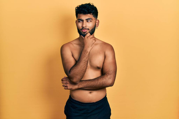 Arab man with beard wearing swimwear shirtless with hand on chin thinking about question, pensive expression. smiling with thoughtful face. doubt concept.  - Photo, Image