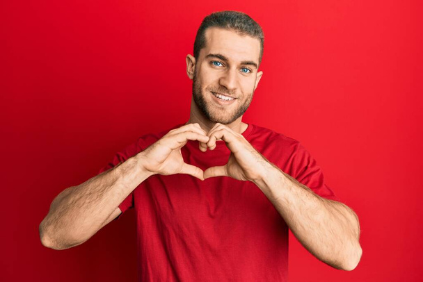 Young caucasian man wearing casual clothes smiling in love doing heart symbol shape with hands. romantic concept.  - Fotoğraf, Görsel
