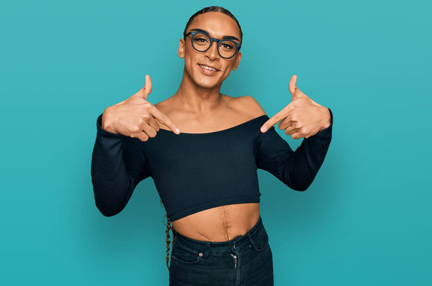 Hispánský transgender muž nosí make-up a dlouhé vlasy nosí ženské oblečení vypadá sebevědomě s úsměvem na tváři, ukazuje sám sebe s prsty hrdý a šťastný.  - Fotografie, Obrázek