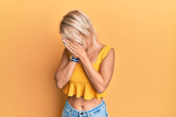 Jong blond meisje draagt casual kleding met droevige uitdrukking bedekken gezicht met handen tijdens het huilen. depressie concept.  - Foto, afbeelding