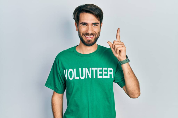 Молодий іспаномовний чоловік у волонтерській сорочці вказує пальцем на успішну ідею. вичерпаний і щасливий. номер один
.  - Фото, зображення
