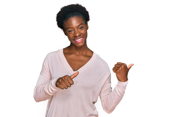 Fiatal afro-amerikai lány alkalmi ruhát visel mutatva a háta mögött a kezét és hüvelykujját fel, mosolygós magabiztos  - Fotó, kép