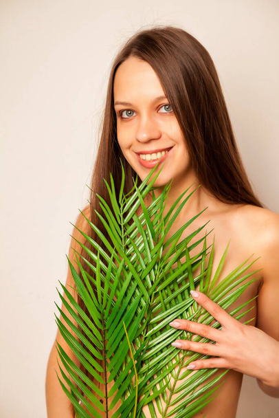 Portrait brunette naked young woman posing with palm leaf and perfect skin in studio, nude makeup over white background. Health care cosmetic procedures concept, beauty and health. Copy space - Foto, immagini