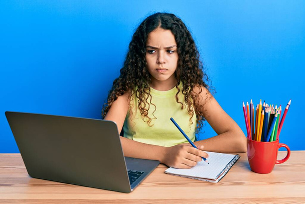 Masada oturan Latin asıllı genç kız okul için çalışıyor şüpheci ve gergin, sorun yüzünden somurtuyor. negatif kişi.  - Fotoğraf, Görsel