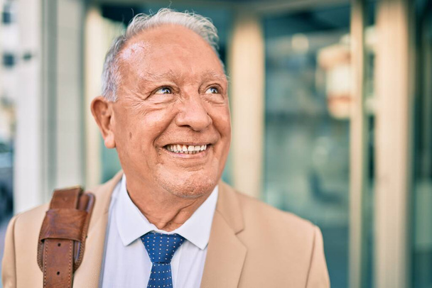 Senior hombre de negocios de pelo gris sonriendo feliz de pie en la ciudad. - Foto, imagen