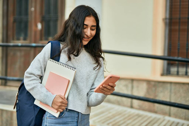 Молодая студентка с Ближнего Востока улыбается счастливой, используя смартфон в городе. - Фото, изображение
