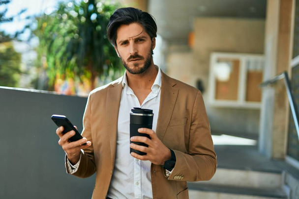 Молодий іспаномовний бізнесмен використовує смартфон і п'є каву в місті
. - Фото, зображення