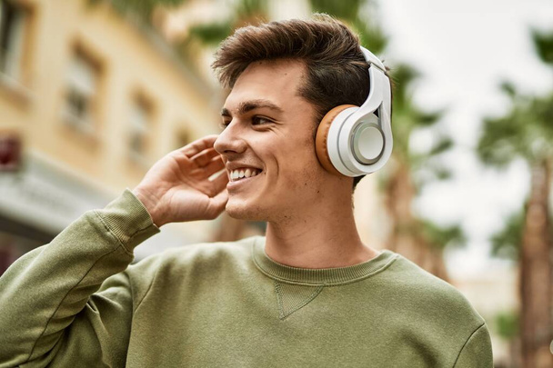 Fiatal spanyol férfi mosolyog boldog használ fejhallgató a városban. - Fotó, kép